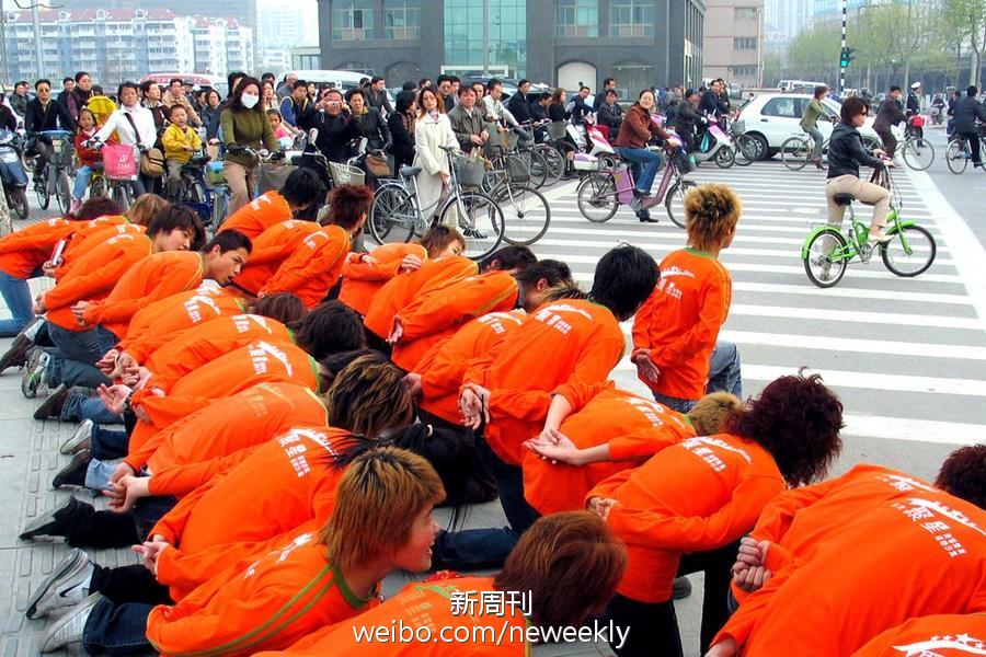 2005年，南京水西门大街一家发廊让新员工们在马路边单膝跪地，弯腰俯首向路人问好。